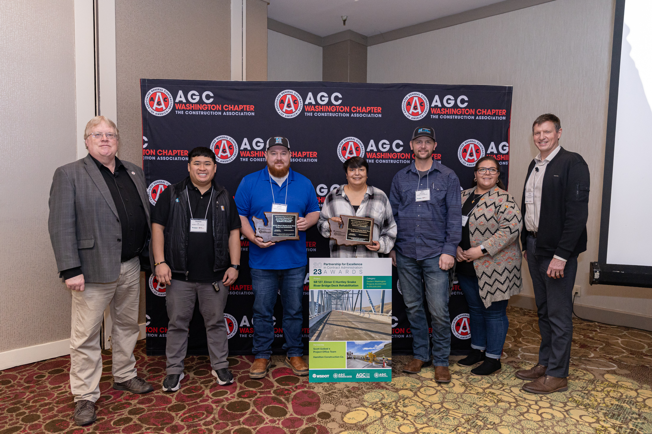 Seven people, two of whom are holding award plaques, standing in front of an AGC Washington Chapter backdrop.