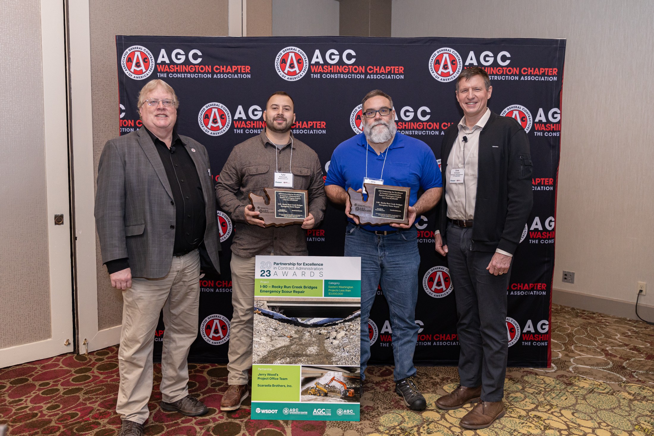 Four people, two of whom are holding award plaques, standing in front of an AGC Washington Chapter backdrop.