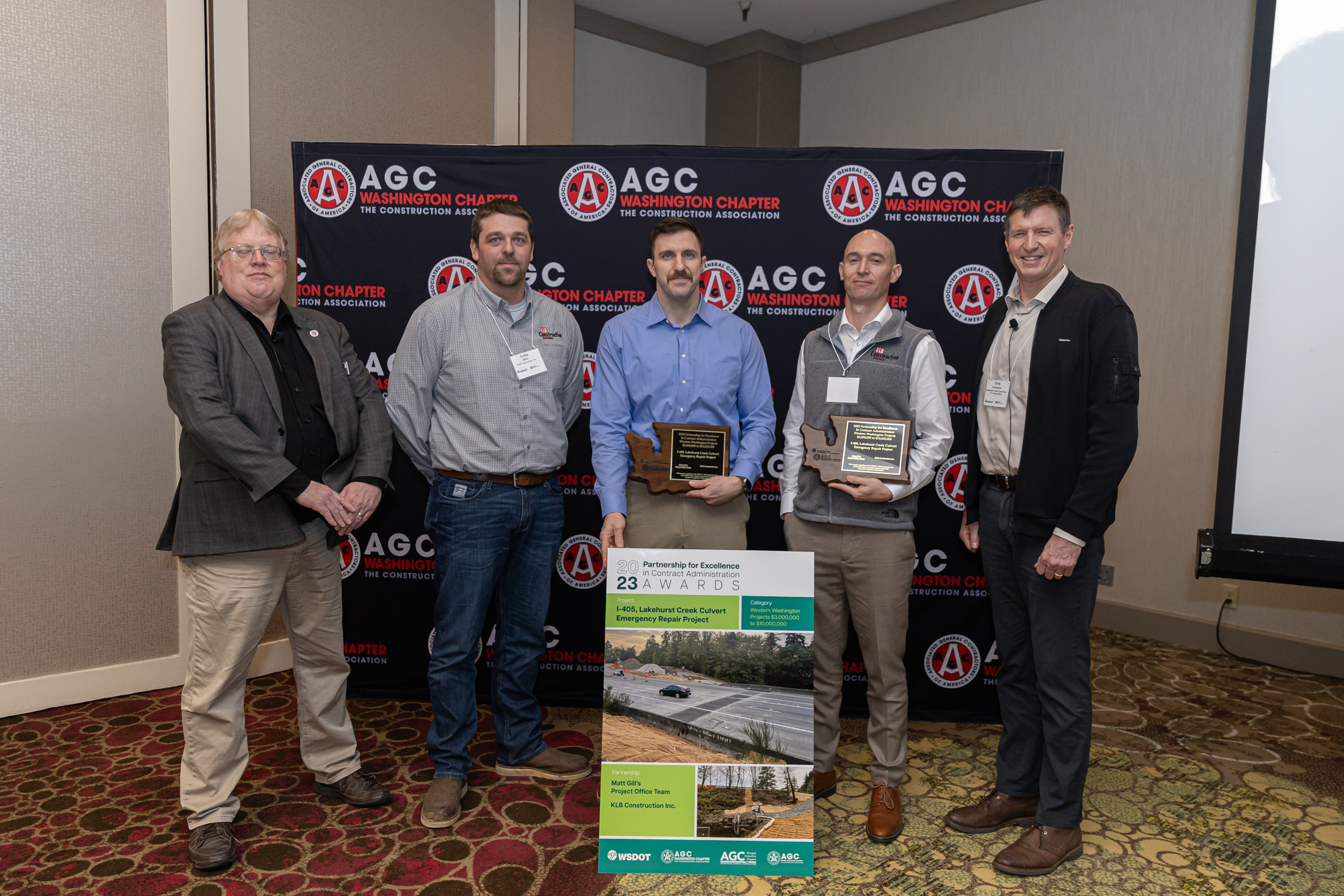 Five people, two of whom are holding award plaques, standing in front of an AGC Washington Chapter backdrop.