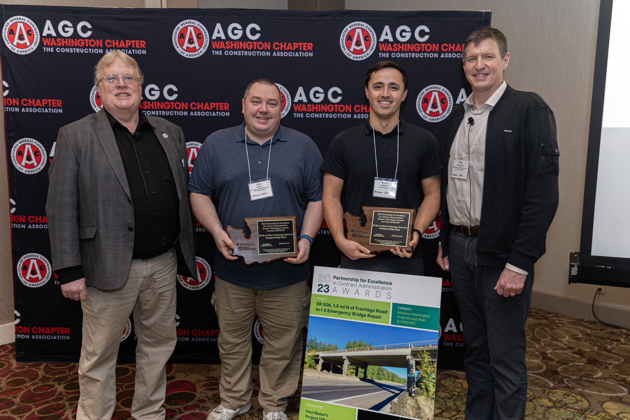 Four people, two of whom are holding award plaques, standing in front of an AGC Washington Chapter backdrop.